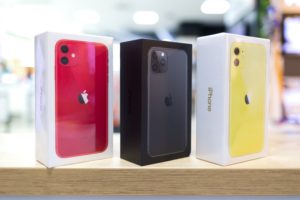 Three white boxe on a light wood countertop, each with a red, black and yellow iPhone pictured on each box respectively