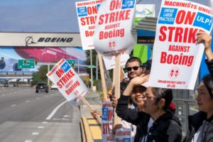 A group of people holding white signs with red writing, alongside a road