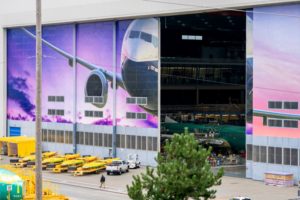 A PARTIALLY OPEN AIRCRAFT MANUFACTURING HANGAR SPORTS HUGE IMAGES OF PLANES ON ITS SLIDING DOORS