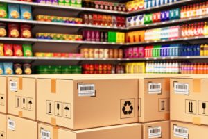 Shelves of multi-colored jars, cartons and potato chip bags, with a stack of brown cardboard boxes in the foreground