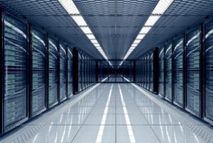 A long hallway with rows of dark-colored computer servers stacked on either side, split by a white linoleum floor