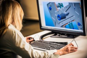 A WOMAN SITS AT A COMPUTER SCREEN, MANIPULATING AN IMAGE OF A MACHINE PART