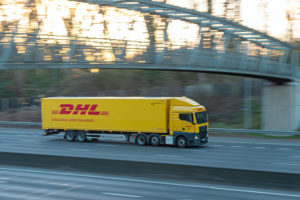 A DHL SUPPLY CHAIN TRUCK SPEEDS ALONG A HIGHWAY TRAVELING UNDER A BRIDGE.