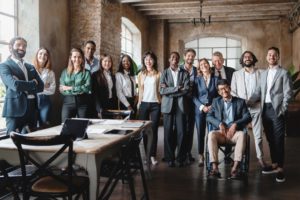 A GROUP OF WORKERS RANGED IN AN OFFICE, OF DIVERSE RACE, GENDER, AGE AND PHYSICAL ABILITY