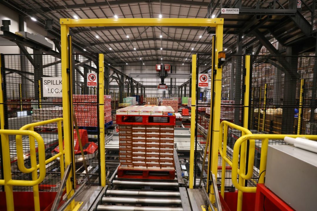 THE INTERIOR OF A WAREHOUSE WITH PALLETS OF GOODS AND BRIGHT YELLOW METAL GUARDRAILS