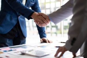 TWO PEOPLE SHAKE HANDS OVER A DESK