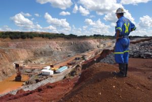 A SUPERVISOR STANDING ON A RIDGE LOOKS DOWN ON MINING OPERATIONS.