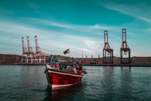 A FISHING BOAT CHUGS AWAY FROM THE PORT OF GWADAR, WITH CRANES VISIBLE ON THE DOCK