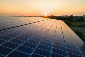 SOLAR PANELS CAN BE SEEN WITH A RISING/SETTING SUN IN THE BACKGROUND.