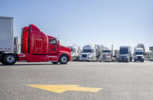 A RED SEMI TRUCK WITH AN EXTENDED CAB APPEARS TO BE PULLING INTO A PARKING LOT FILLED WITH OTHER SEMI-TRAILER TRUCKS.