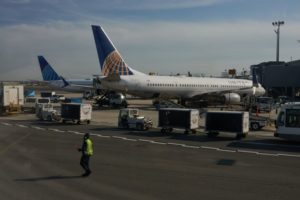 A WORKER IN HI-VIS VEST CROSSES THE TARMAC OF AN AIRPORT WITH TWO UNITED PLANES PARKED IN THE BACKGROUND