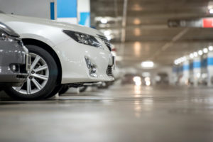 THE FRONT END OF A WHITE CAR PEAKS OUT OF A PARKING SPACE IN AN UNDERGROUND LOT.