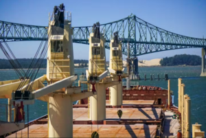 A view from aboard a container ship with four masts, with a large blue span bridge in the background